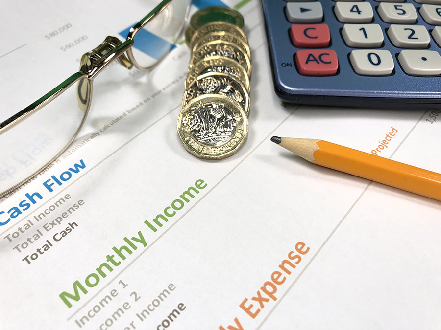 Calculator, coins, glasses and pen sat on top of cashflow, income and expenses forms.